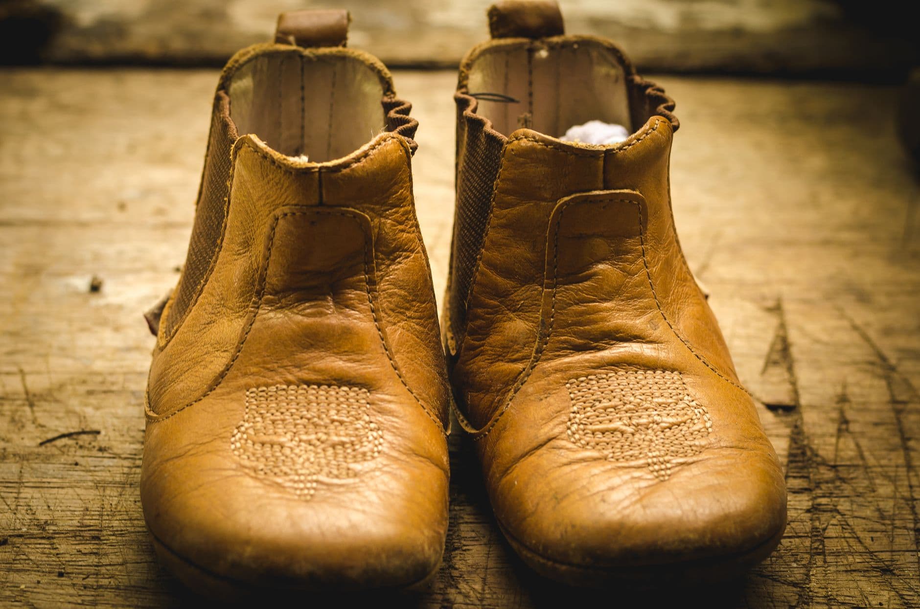 A pair of worn moc-toe leather boots on a wooden surface