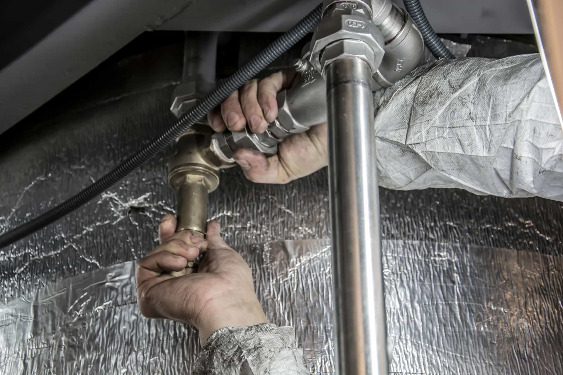 A plumber working on pipework under a sink