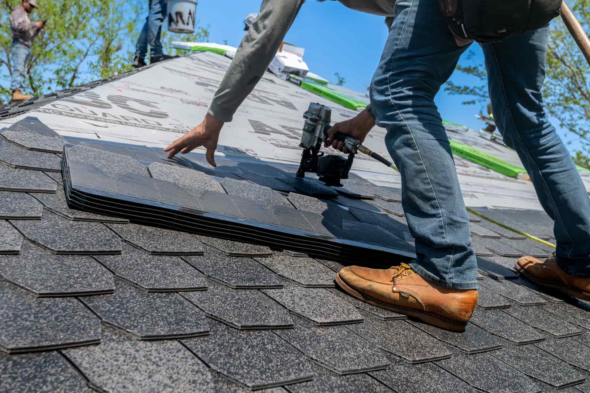 A roofer working on a steeply pitched shingle roof