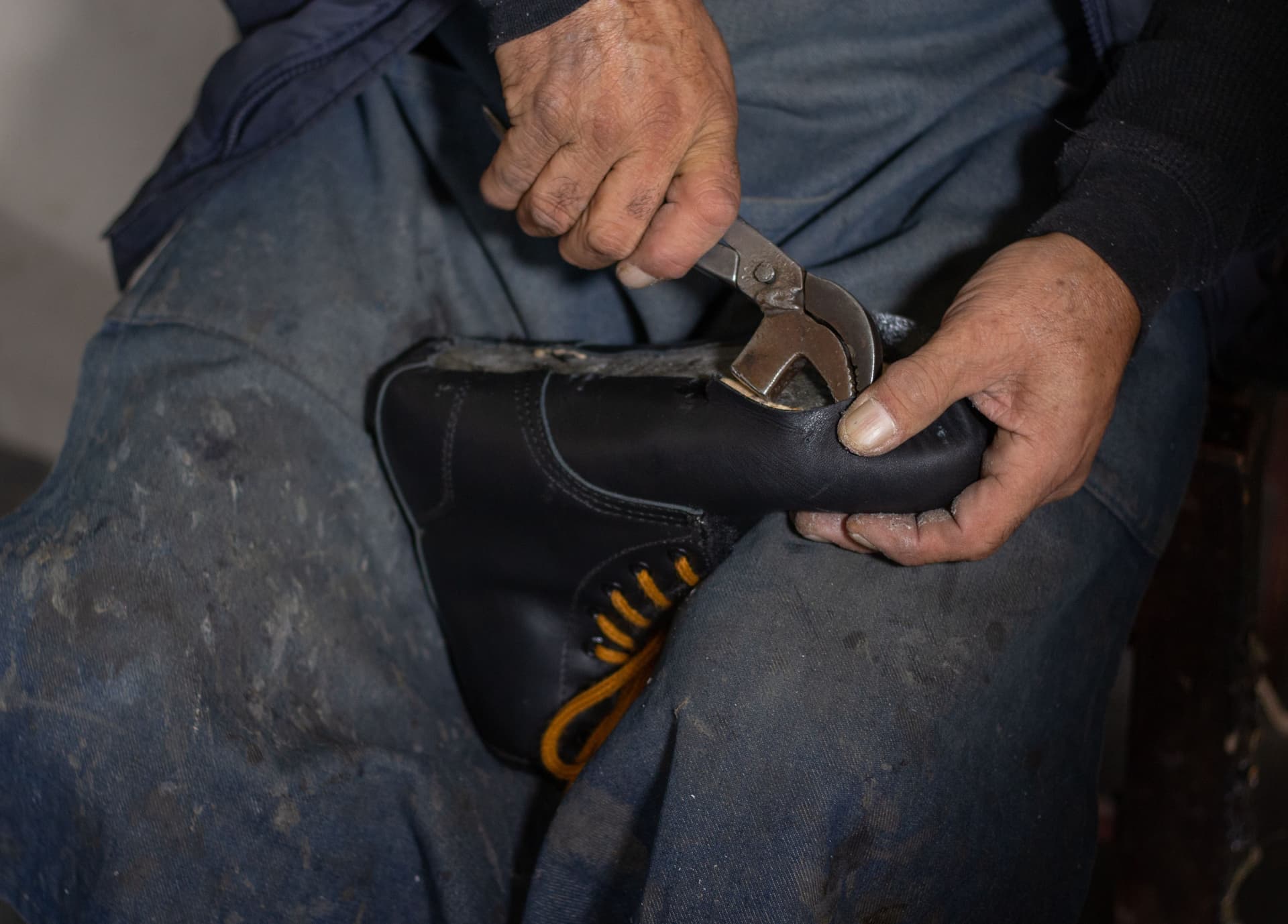 A bootmaker stitching a leather upper at a workbench